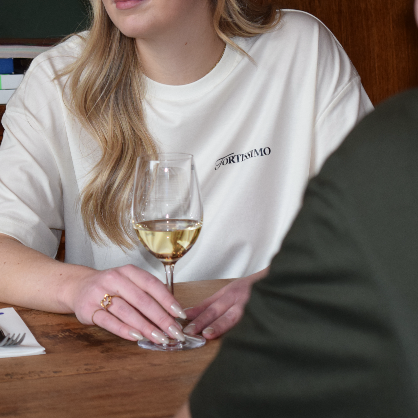 a women in a restaurant setting, showing the front of the Fortissimo Fontana di Trevi shirt in creme.