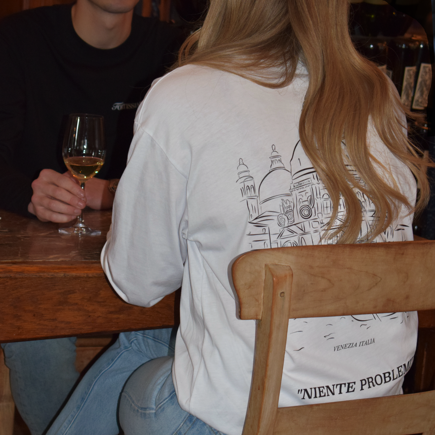 Woman and men in a restaurant setting, showing the back of the white Venezia Longsleeve.