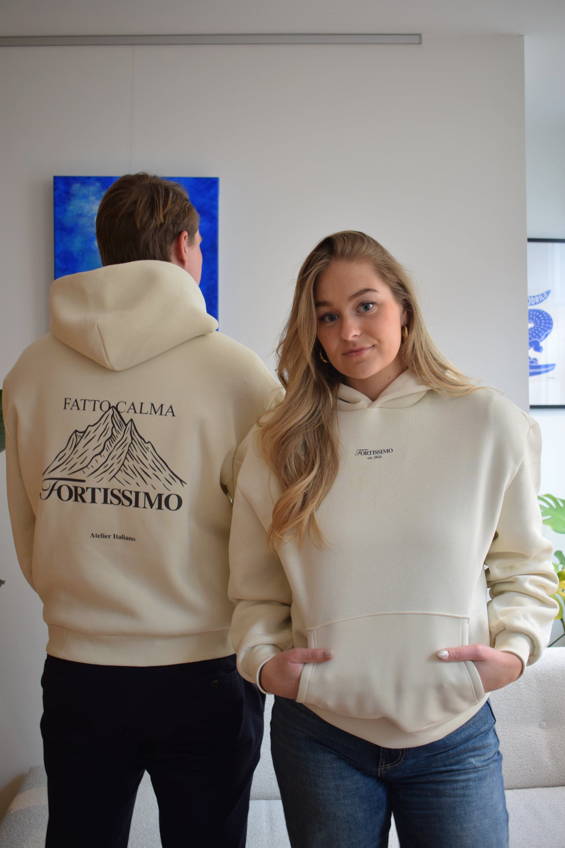 Two people wearing cream hoodies with text and graphics, one facing away showing text on the back.